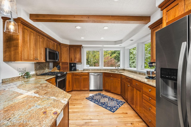 kitchen featuring light stone countertops, light wood-type flooring, brown cabinets, a sink, and stainless steel appliances