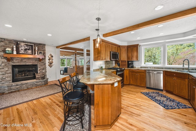 kitchen with brown cabinets, a sink, a textured ceiling, stainless steel appliances, and a peninsula