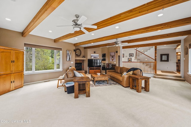carpeted living area with a ceiling fan, beam ceiling, stairway, a glass covered fireplace, and recessed lighting