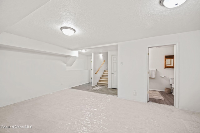 finished basement featuring stairs, a textured ceiling, and baseboards