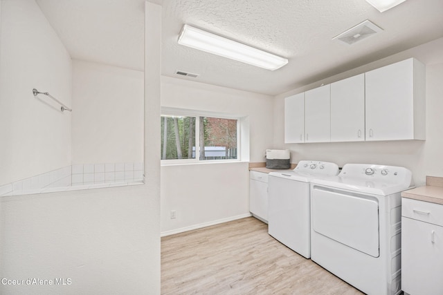 laundry room with visible vents, washer and clothes dryer, cabinet space, and light wood finished floors