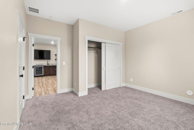 unfurnished bedroom featuring visible vents, a closet, light carpet, and beverage cooler