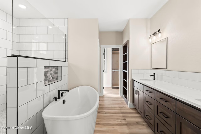 full bathroom featuring double vanity, a freestanding tub, wood finished floors, recessed lighting, and a sink