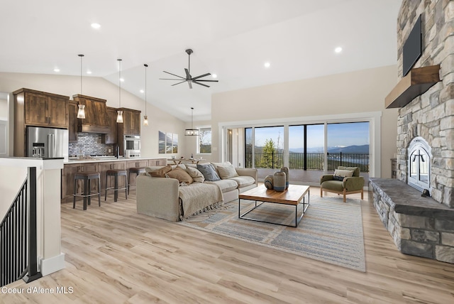 living room with high vaulted ceiling, a ceiling fan, light wood-type flooring, and a stone fireplace