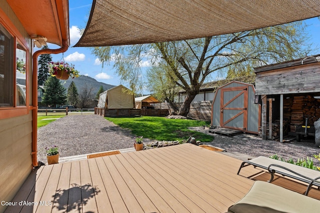 deck with a fenced backyard, a storage unit, a mountain view, and an outbuilding