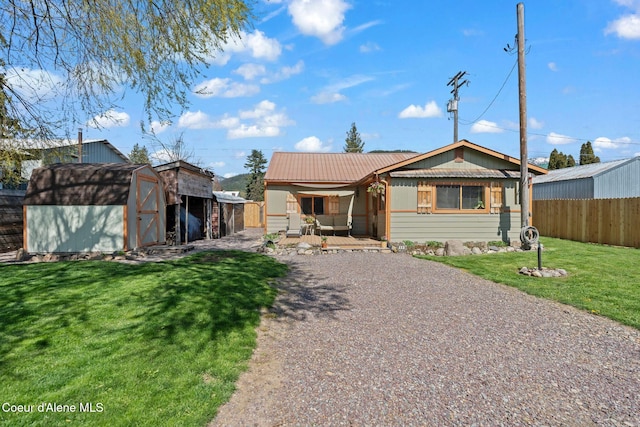 bungalow-style home with an outdoor structure, fence, a front yard, a storage unit, and metal roof