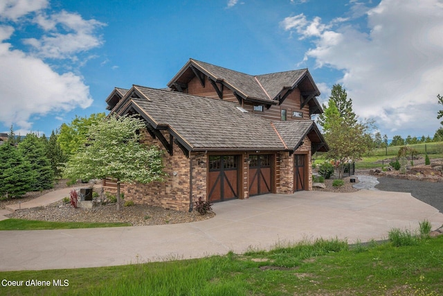 view of property exterior with a garage, fence, stone siding, and concrete driveway
