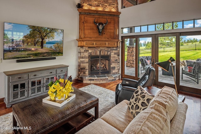 living room with baseboards, a stone fireplace, wood finished floors, and a towering ceiling