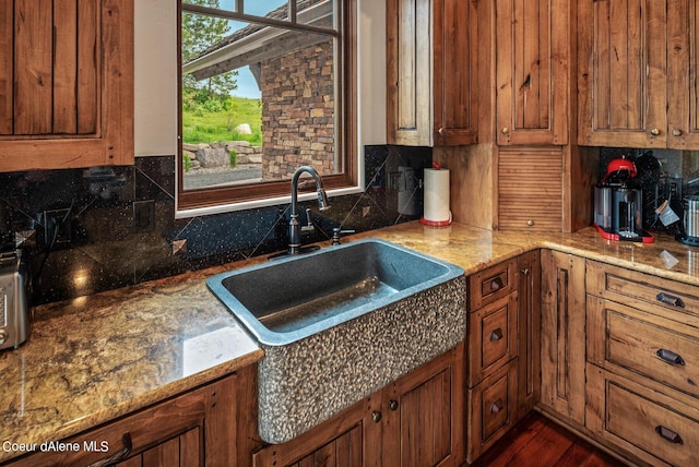 kitchen featuring a sink, decorative backsplash, brown cabinetry, and light stone countertops