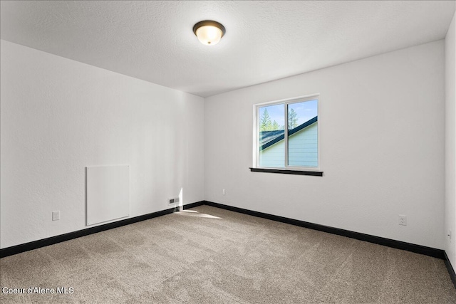 carpeted spare room featuring a textured ceiling and baseboards