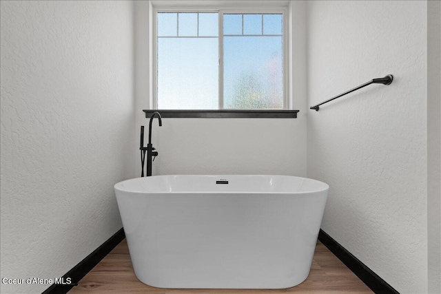 full bath with baseboards, a textured wall, and a wealth of natural light
