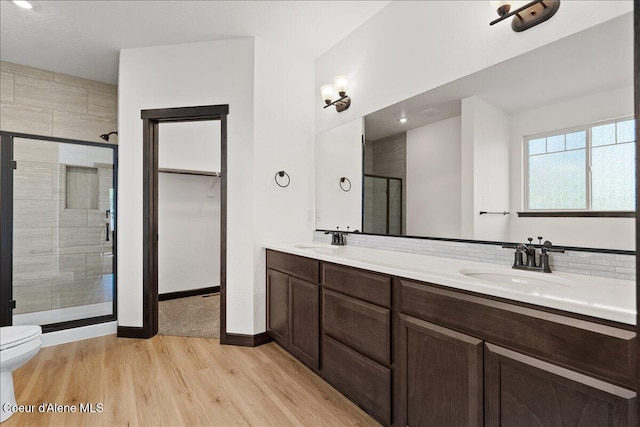 bathroom featuring wood finished floors, a sink, a stall shower, and double vanity