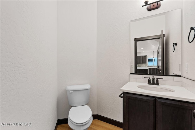 half bath with a textured wall, vanity, toilet, wood finished floors, and backsplash