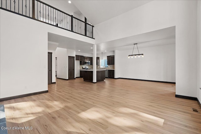 unfurnished living room featuring a chandelier, baseboards, visible vents, and light wood-style flooring