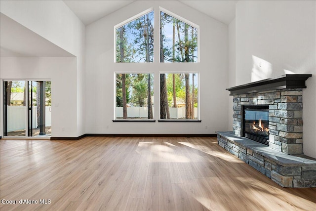 unfurnished living room with baseboards, high vaulted ceiling, a stone fireplace, and a healthy amount of sunlight
