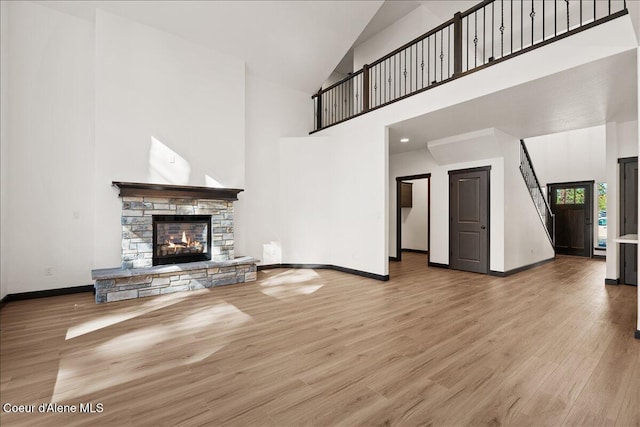 unfurnished living room featuring baseboards, a fireplace, wood finished floors, and high vaulted ceiling