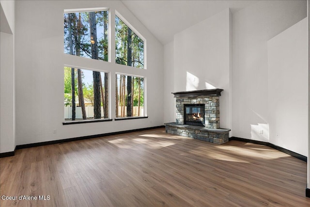 unfurnished living room featuring high vaulted ceiling, a stone fireplace, baseboards, and wood finished floors