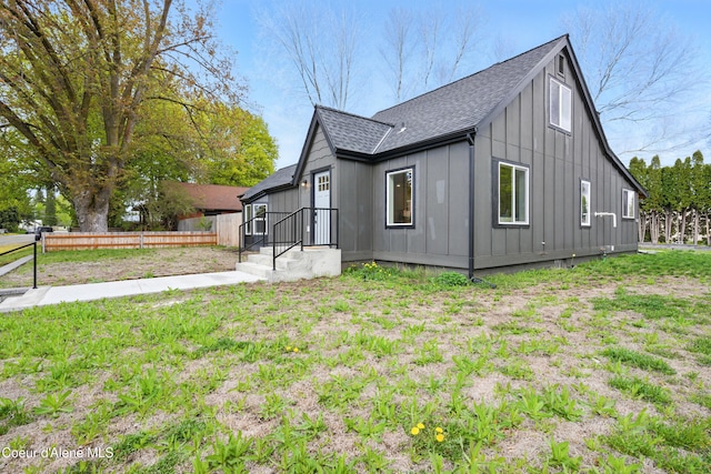 view of home's exterior featuring a lawn, a shingled roof, board and batten siding, and fence