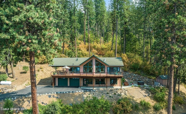rear view of property with an outdoor structure, driveway, a deck, an attached garage, and a storage shed