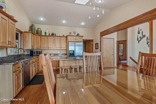kitchen featuring vaulted ceiling with skylight, appliances with stainless steel finishes, a center island, light wood-type flooring, and dark stone countertops