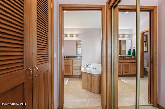 full bath featuring toilet, two vanities, tile patterned flooring, and a garden tub