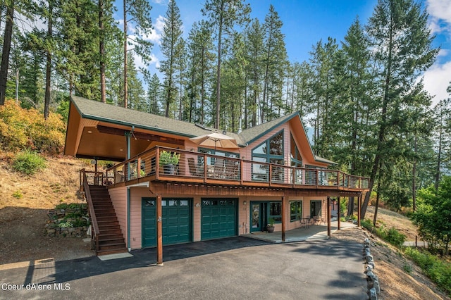 rear view of property featuring a garage, a wooden deck, stairs, and aphalt driveway
