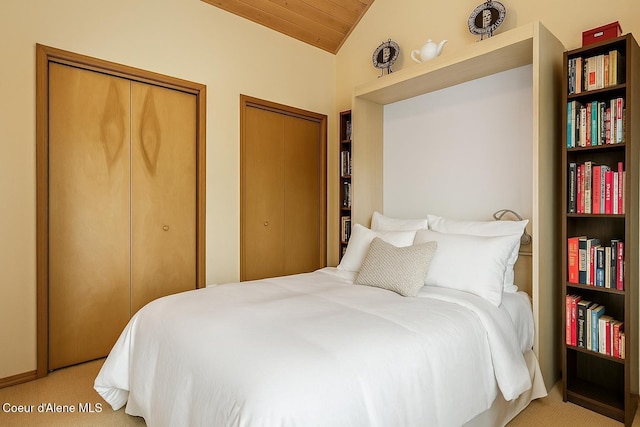 bedroom featuring vaulted ceiling, wooden ceiling, light carpet, and two closets