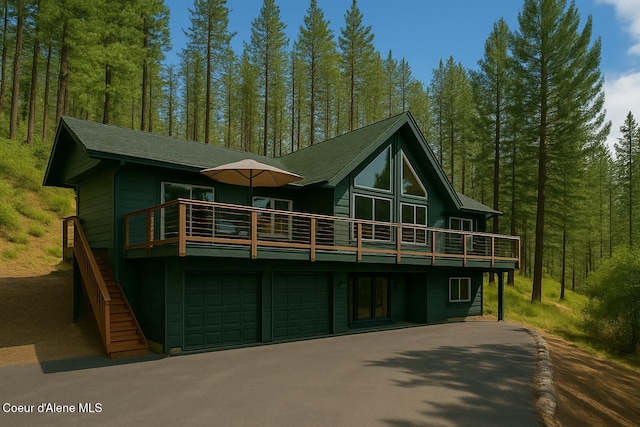 back of house with a view of trees, an attached garage, a deck, and aphalt driveway