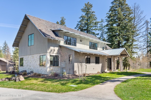 modern inspired farmhouse featuring a shingled roof, stone siding, and a front yard