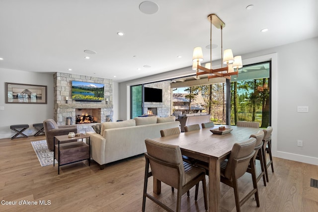 dining area with a stone fireplace, recessed lighting, an inviting chandelier, and light wood-type flooring