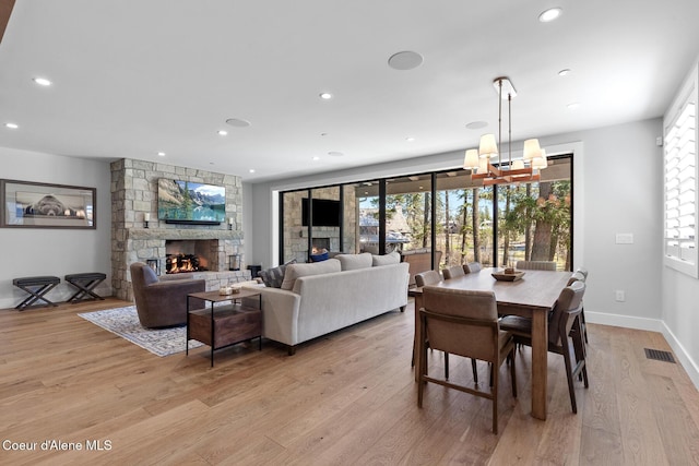 dining area with an inviting chandelier, light wood finished floors, a stone fireplace, recessed lighting, and visible vents
