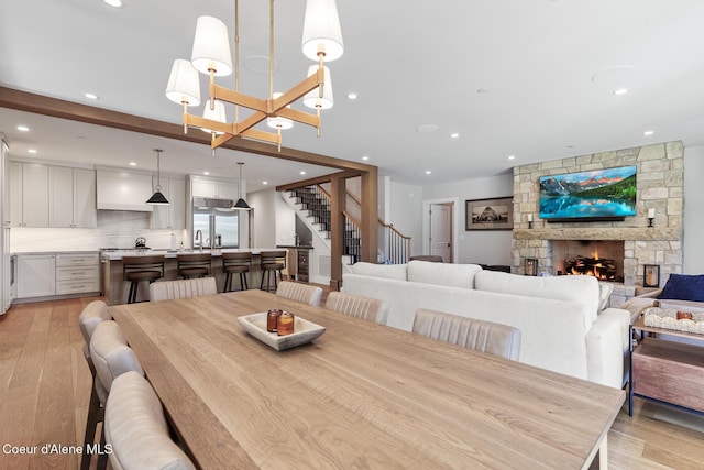 dining room with light wood-style floors, recessed lighting, stairs, and a stone fireplace