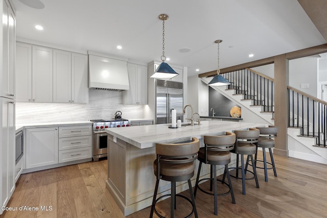 kitchen featuring a sink, high end appliances, premium range hood, and light wood-style flooring