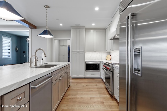 kitchen featuring a sink, built in appliances, recessed lighting, decorative light fixtures, and light wood-type flooring