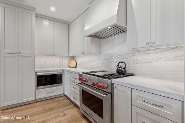 kitchen with light stone counters, built in microwave, designer range, custom range hood, and backsplash