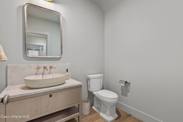 half bathroom featuring toilet, baseboards, wood finished floors, and vanity