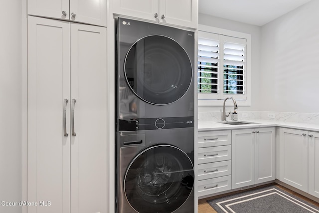washroom with a sink, cabinet space, stacked washing maching and dryer, and wood finished floors