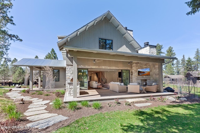 rear view of house featuring stone siding, a ceiling fan, a chimney, and an outdoor living space with a fireplace