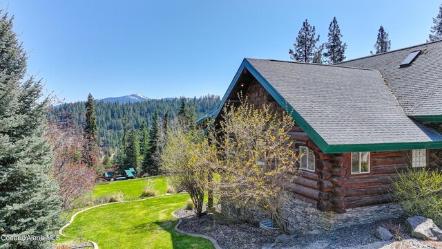 122 Makridge Ln, Kingston, ID 83839 - view of home's exterior with stone siding, roof with shingles, log siding, a view of trees, and a yard
