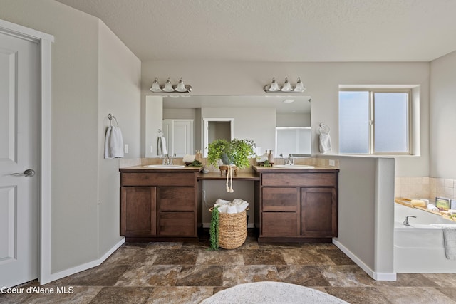 9362 N Prince William Loop, Hayden, ID 83835 - bathroom featuring baseboards, two vanities, a bath, stone finish floors, and a textured ceiling