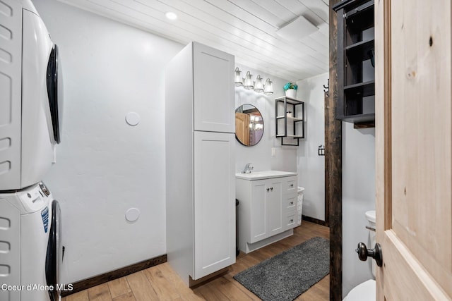bathroom featuring vanity, wood finished floors, toilet, stacked washing maching and dryer, and wooden ceiling