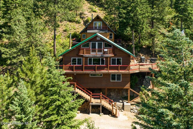 rear view of house featuring a wooden deck, a view of trees, stairs, and a balcony