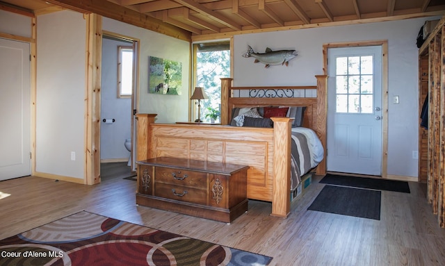 bedroom featuring baseboards, wood finished floors, and beam ceiling