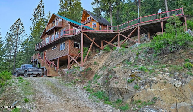 back of property with a wooden deck, stairs, and dirt driveway