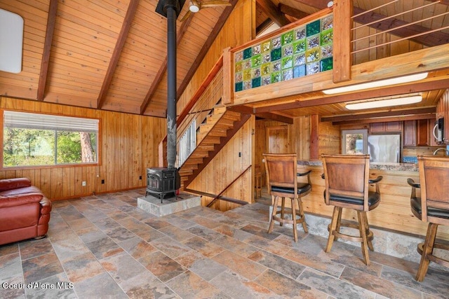 living room with a wood stove, beam ceiling, wooden ceiling, stone tile flooring, and wooden walls
