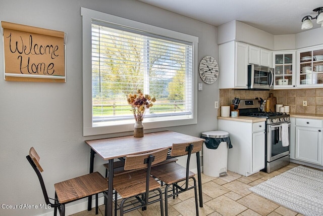 kitchen featuring stainless steel appliances, backsplash, light countertops, glass insert cabinets, and white cabinets