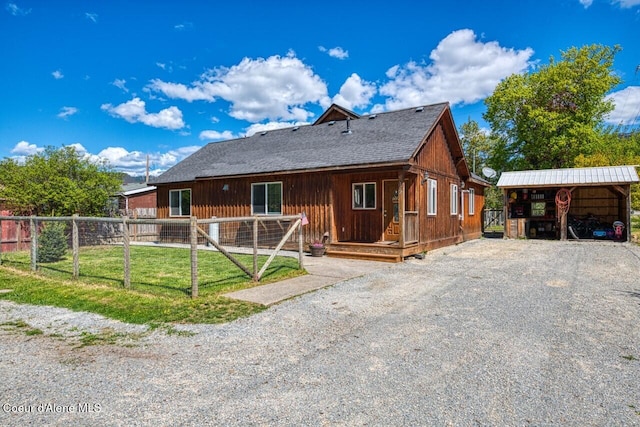 rear view of property with gravel driveway, fence, and a detached carport