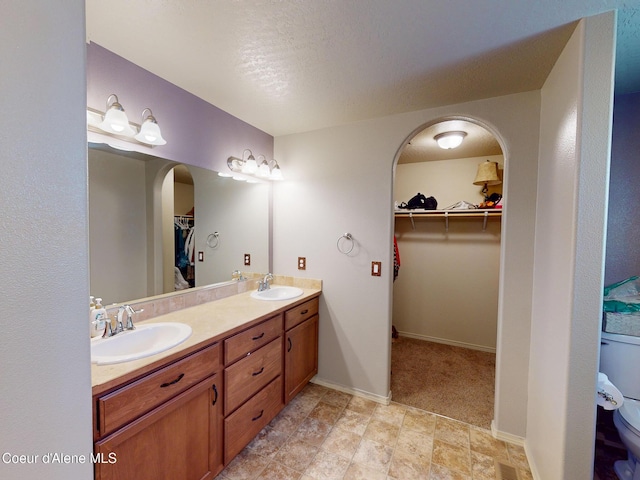 bathroom with a sink, a walk in closet, baseboards, and double vanity