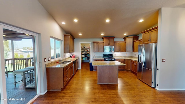 kitchen with a kitchen island, appliances with stainless steel finishes, vaulted ceiling, wood finished floors, and a sink