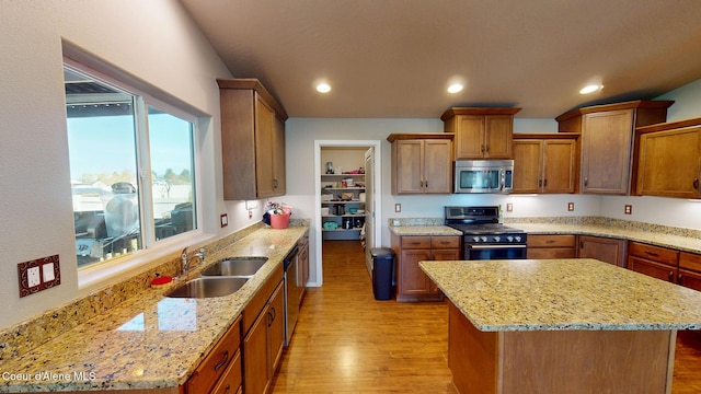 kitchen featuring stainless steel appliances, light stone counters, a sink, and light wood-style flooring